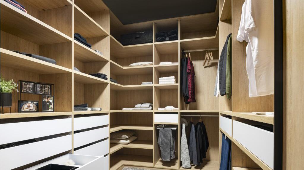 Inloopkast met houten planken en laden, kleding netjes opgehangen en opgevouwen.