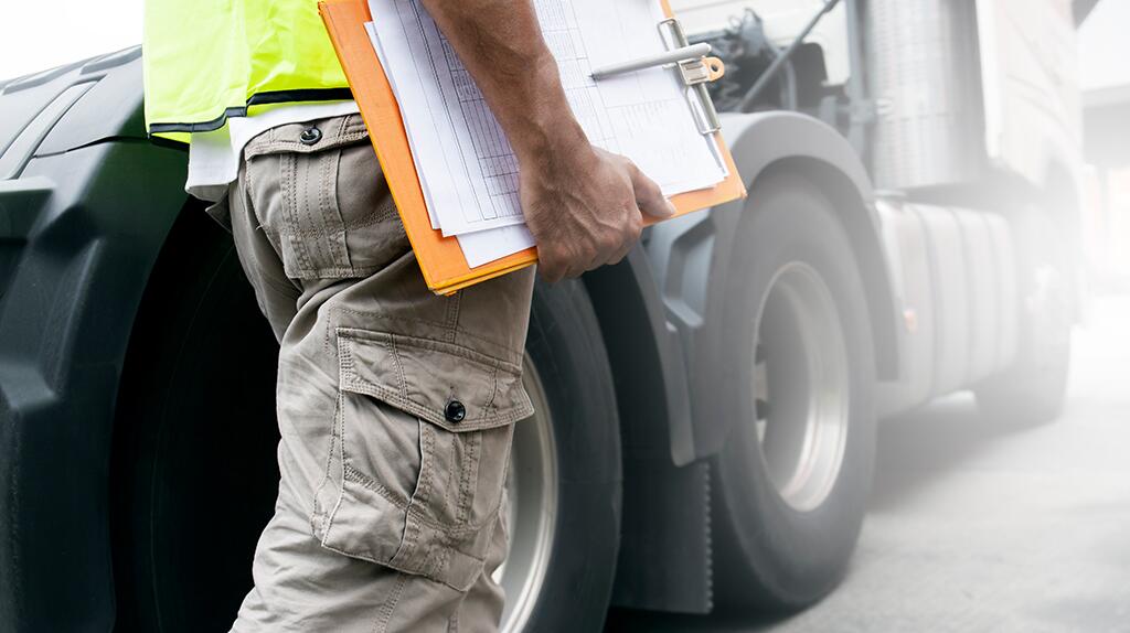 Man met clipboard naast vrachtwagenband.