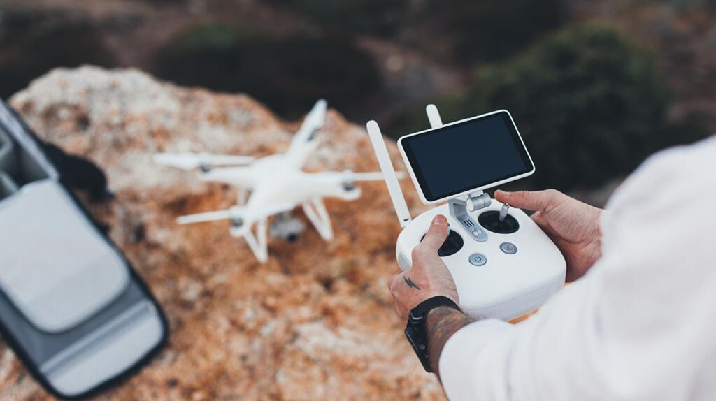 Handen besturen een drone met een afstandsbediening op een rotsachtige ondergrond.