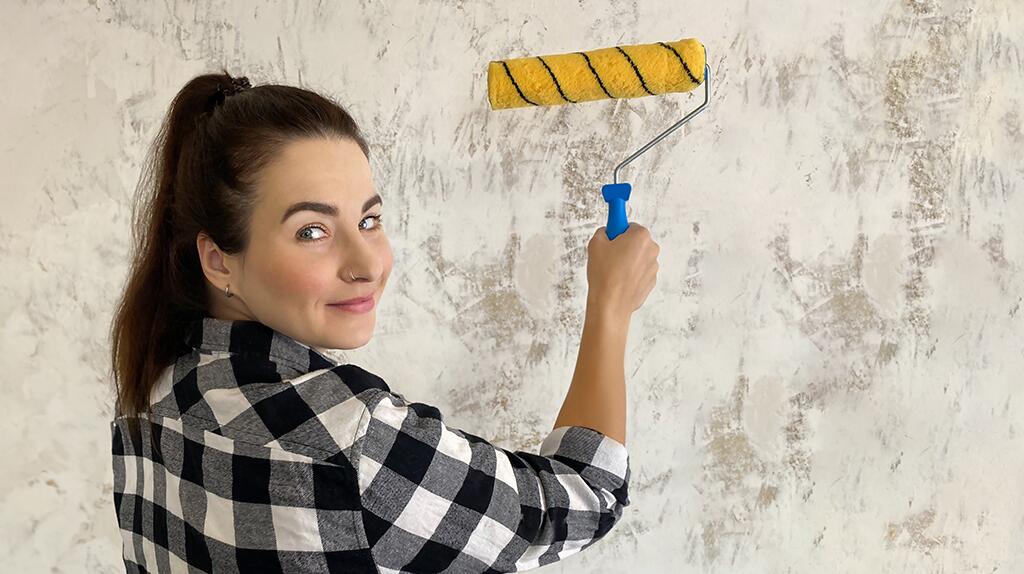 Vrouw met zwart-wit geruit shirt schildert muur met gele roller.