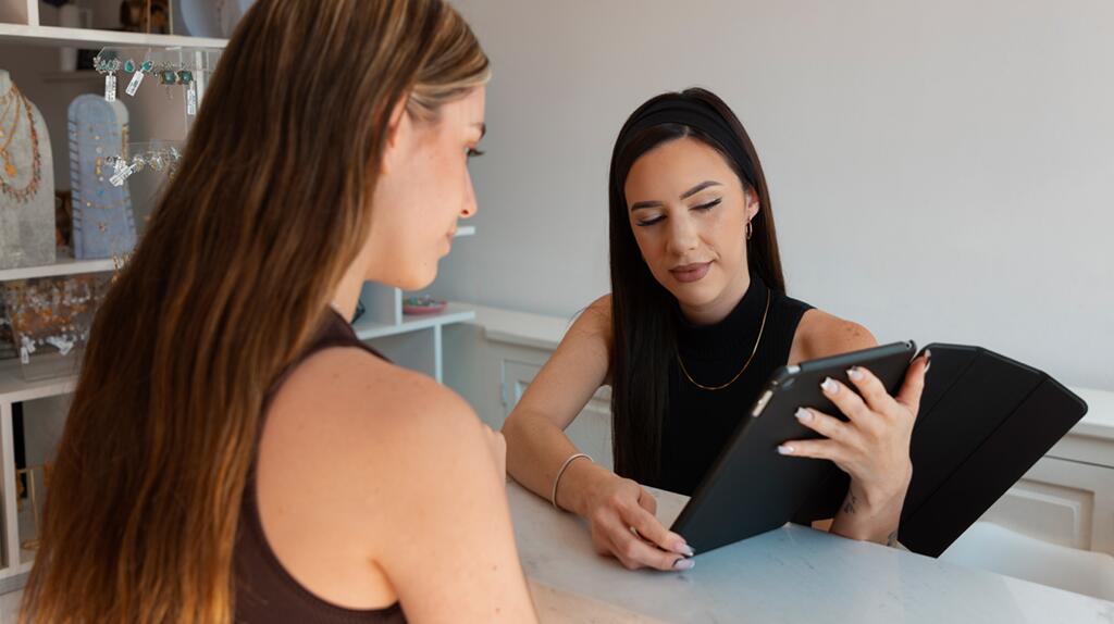 Twee vrouwen bespreken iets op een tablet aan een bureau.