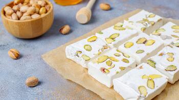 Zachte nougatrepen met pistachenoten op bakpapier, naast een kom noten en een houten lepel.