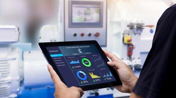Tablet met grafieken en gegevens in een fabrieksomgeving.