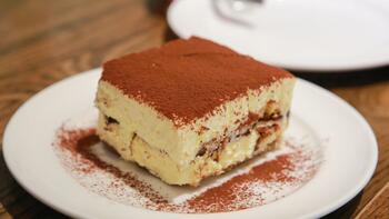 Tiramisu op een wit bord, gestrooid met cacaopoeder.