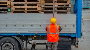 Persoon in oranje veiligheidskleding staat bij een vrachtwagen vol pallets.