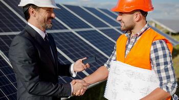 Twee mannen met helmen schudden handen bij zonnepanelen.