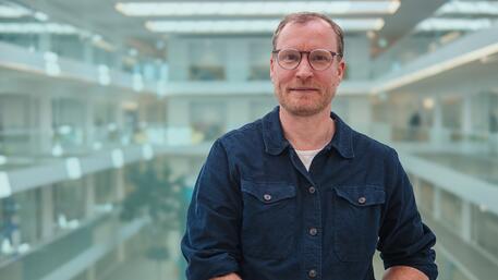 Man met bril in een kantoorruimte met glazen balustrades.