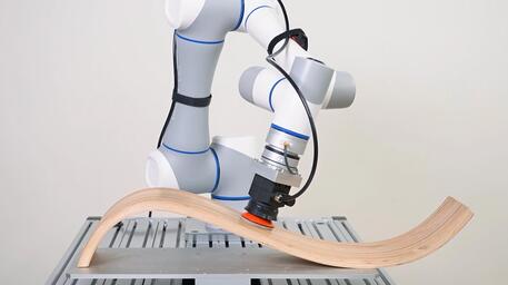 Robotarm bewerkt een gebogen houten stuk op een werkblad.