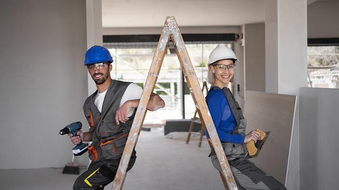 Twee bouwvakkers op een ladder met helmen in een onafgemaakte ruimte.