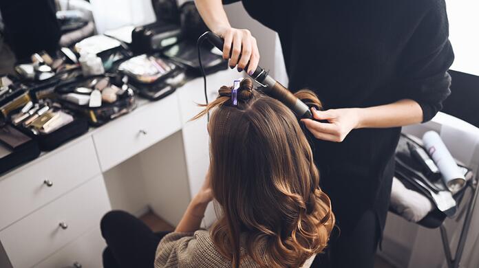 Vrouw krijgt krullen met stijltang in kapsalon.