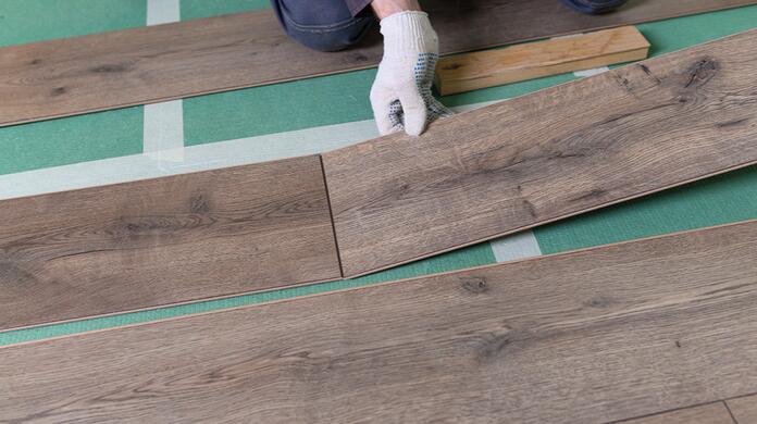 Laminaatvloer leggen met handschoenen op groene ondervloer.