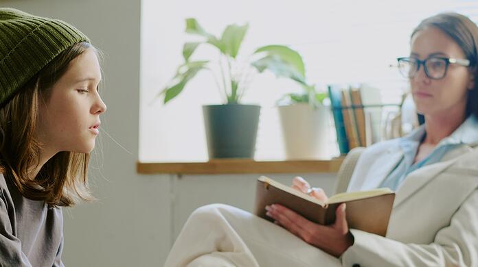 Therapeut in gesprek met jong meisje in kamer, planten op achtergrond.