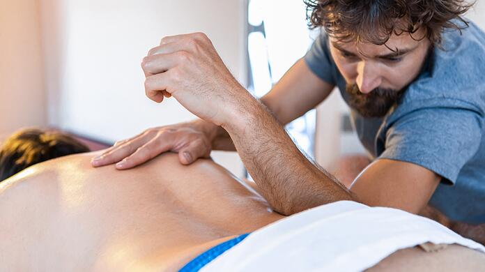Masseur behandelt rug van een persoon in een rustige ruimte.