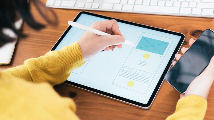Hand tekent ontwerp op tablet; smartphone in andere hand.