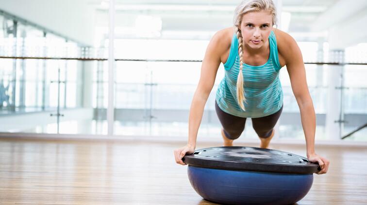 Vrouw doet plank op een bosubal in een sportschool.