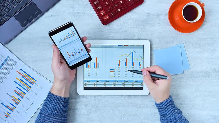 Tablet en smartphone met grafieken op een bureau, naast een kop koffie.