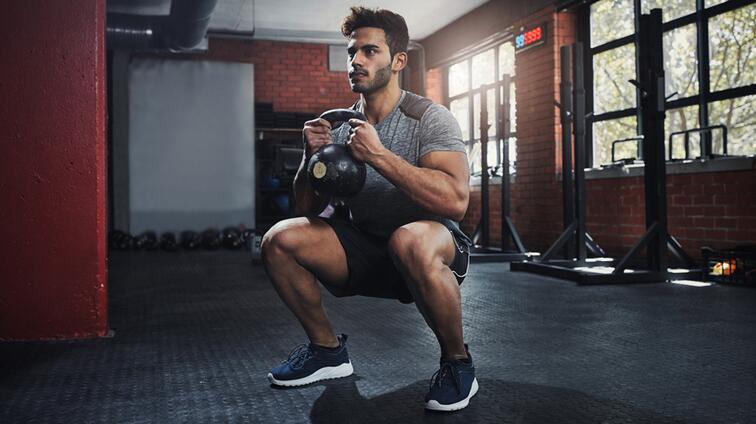 Man squattend met kettlebell in sportschool.