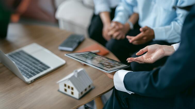 Persoon in pak toont tablet tijdens zakelijke bespreking aan tafel.