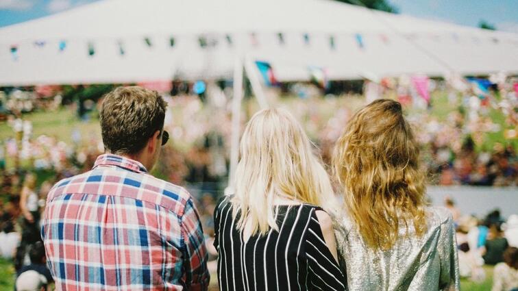 Drie mensen van achteren bekeken tijdens een buitenfestival, met een tent op de achtergrond.