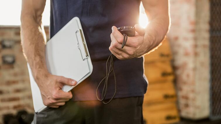 Man met clipboard en stopwatch in sportschool.