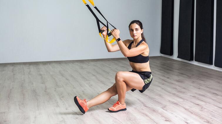Vrouw doet TRX-oefening in fitnessruimte.
