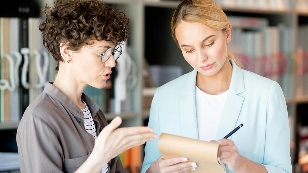 Twee vrouwen bespreken notities in een kantooromgeving.